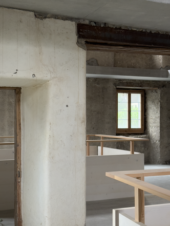 Roh belassener Innenraum mit historischen Wänden, sichtbarem Deckenbalken und neuen Einbauten aus Holz.