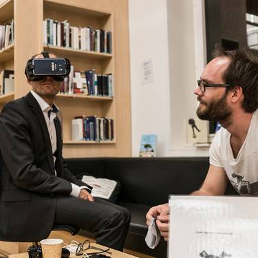 Blick auf zwei Personen sitzen bei einer Veranstaltung in der Bibliothek, einer trägt eine Virtual Reality Brille