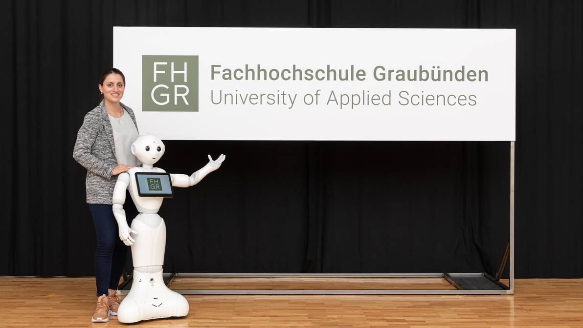 Digital-Business-Management-Studentin Mara Carl und Pepper präsentieren das Logo der FH Graubünden.