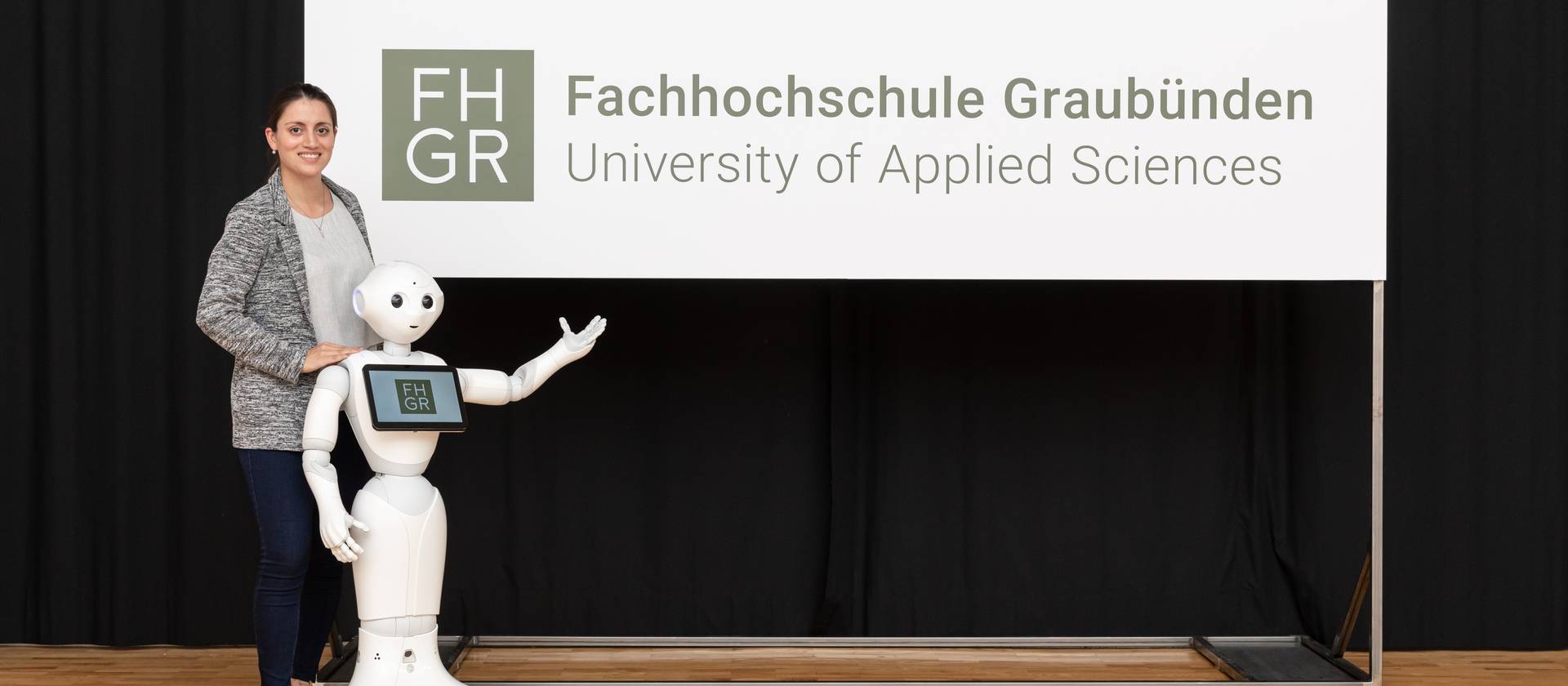 Enthüllung Logo FH Graubünden Digital-Business-Management-Studentin Mara Carl und Pepper präsentieren das Logo der FH Graubünden.