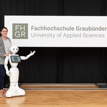 Digital-Business-Management-Studentin Mara Carl und Pepper präsentieren das Logo der FH Graubünden.