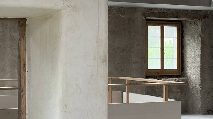Wer hier studiert, gestaltet Räume, die schon da sind. Roh belassener Innenraum mit historischen Wänden, sichtbarem Deckenbalken und neuen Einbauten aus Holz.