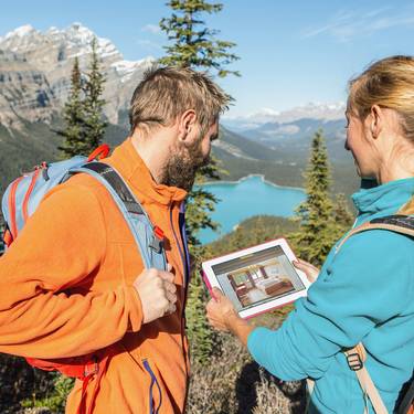 Imagebild Zwei Wanderer halten ein Tablet mit Blick auf einen Bergsee.