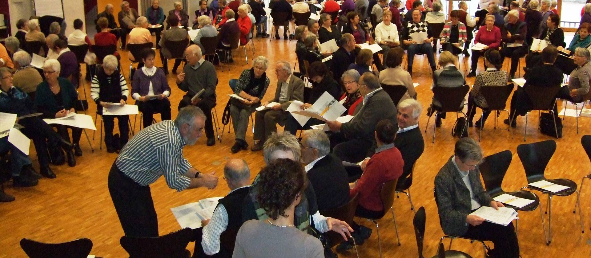 Ältere Personen die auf Stühlen sitzen und Blätter auf dem Schoss haben
