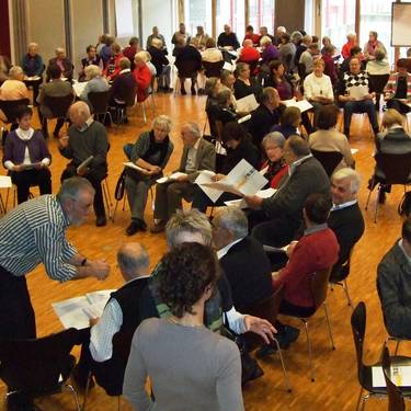 Ältere Personen die auf Stühlen sitzen und Blätter auf dem Schoss haben