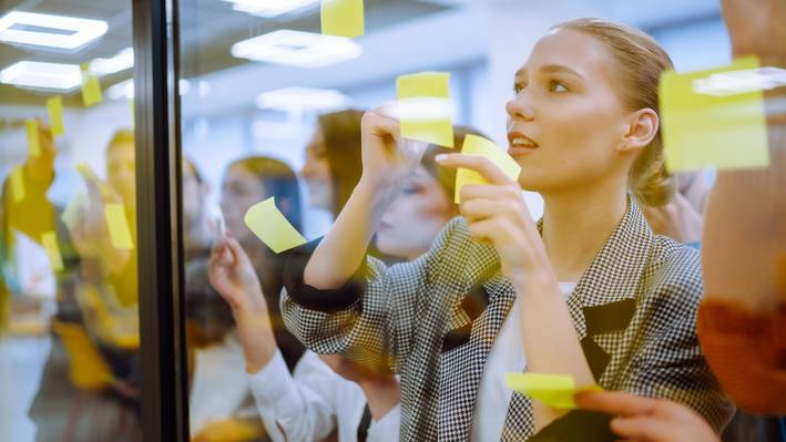 Eine junge Berufstätige Frau arbeitet an einer Glaswand voller Post-it-Notizen