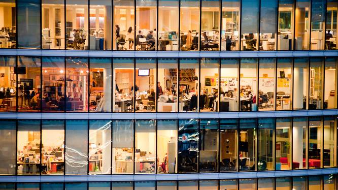 Mehrstöckiges, warm beleuchtetes Bürogebäude mit Glasfront