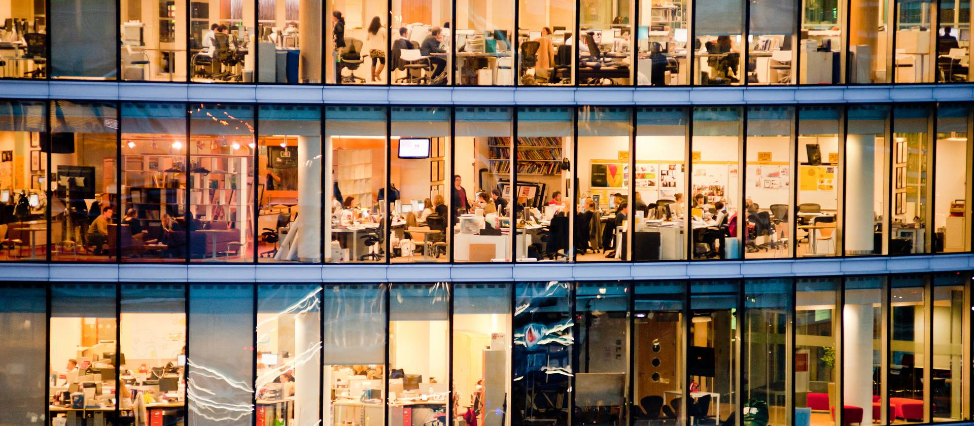 Mehrstöckiges, warm beleuchtetes Bürogebäude mit Glasfront