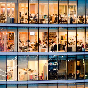 Mehrstöckiges, warm beleuchtetes Bürogebäude mit Glasfront