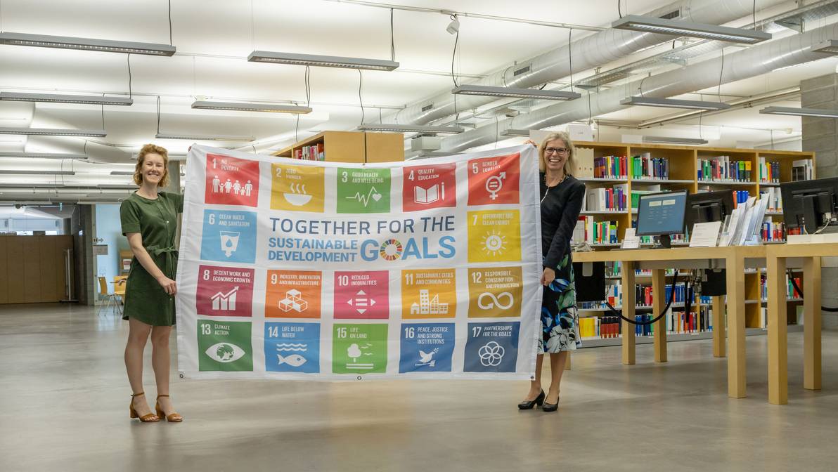 Prof. Dr. Ulrike Zika (rechts) und Eleanor Jehan (links) halten die SDG-Fahne hoch und setzen sich für eine Nachhaltige Entwicklung an der FH Graubünden ein.