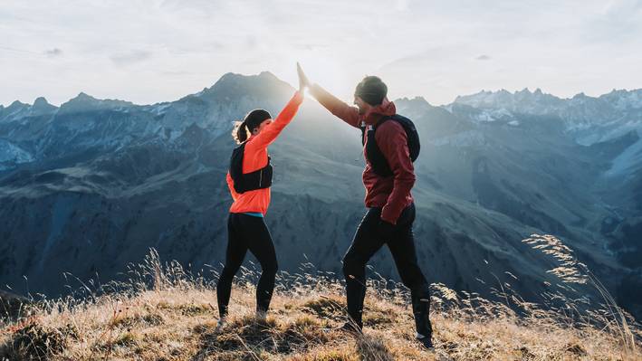 Zwei Trailrunner klatschen sich auf einem Bergkamm im Gegenlicht ab, im Hintergrund die Bündner Bergwelt.
