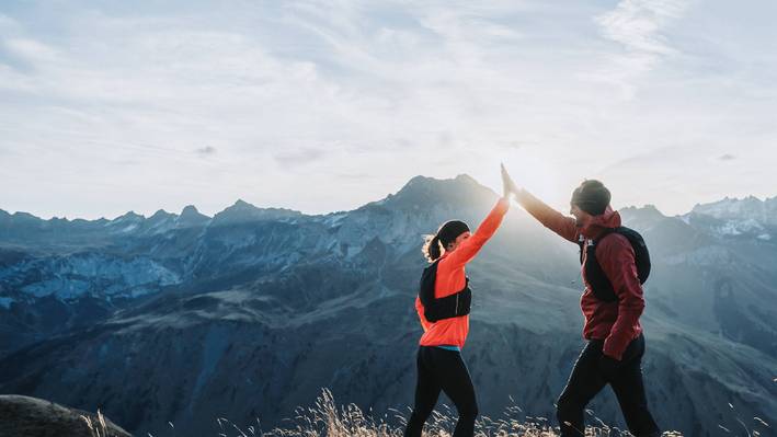 Wer hier studiert, denkt über das eigene Fach hinaus. Zwei Trailrunner klatschen sich auf einem Bergkamm im Gegenlicht ab, im Hintergrund die Bündner Bergwelt.