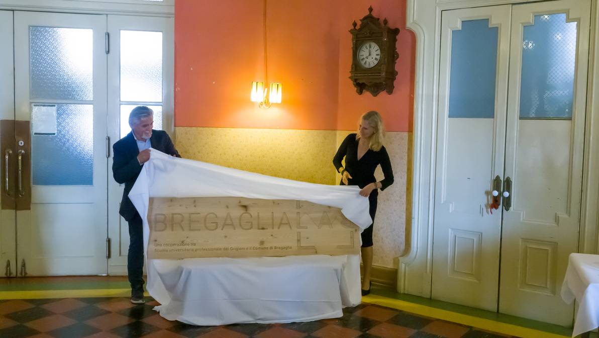 Das Logo des Bregaglia Lab wird von Fernando Giovanoli, Gemeindepräsident Bregaglia, und Ulrike Zika, Departementsleiterin FH Graubünden, enthüllt.