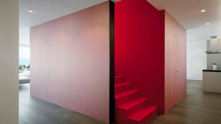 Wer hier studiert, stellt sich gerne hohen Anforderungen. Raumhoher roter Einbau mit Treppe in einem hellen Wohnraum.
