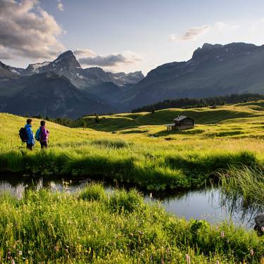 Eine Frau und ein Mann blicken beim Wandern auf die von der Sonne belichteten Natur der Alp Flix. 