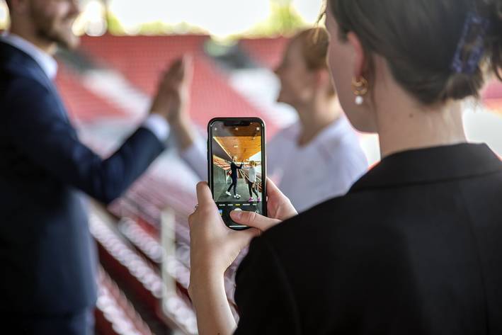 Frau fotografiert Studierende mit dem Smartphone.