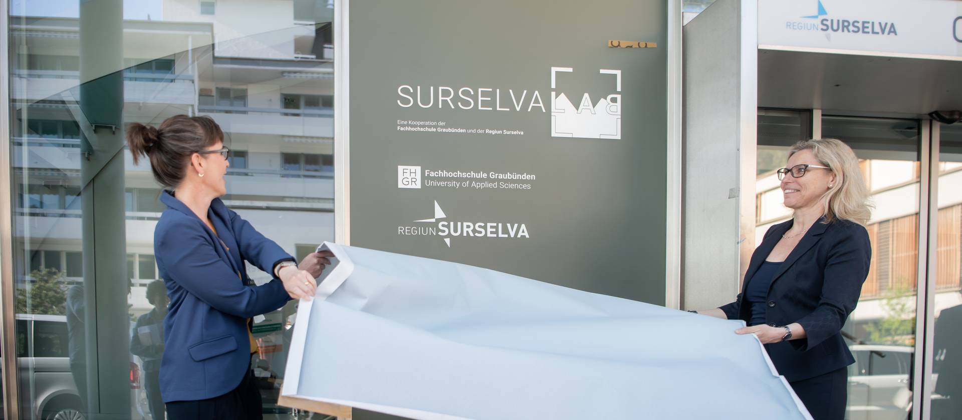 Carmelia Maissen, als Vertreterin der Surselva, und Ulrike Zika, als Vertreterin der FH Graubünden, enthüllen das Logo des Surselva Lab.