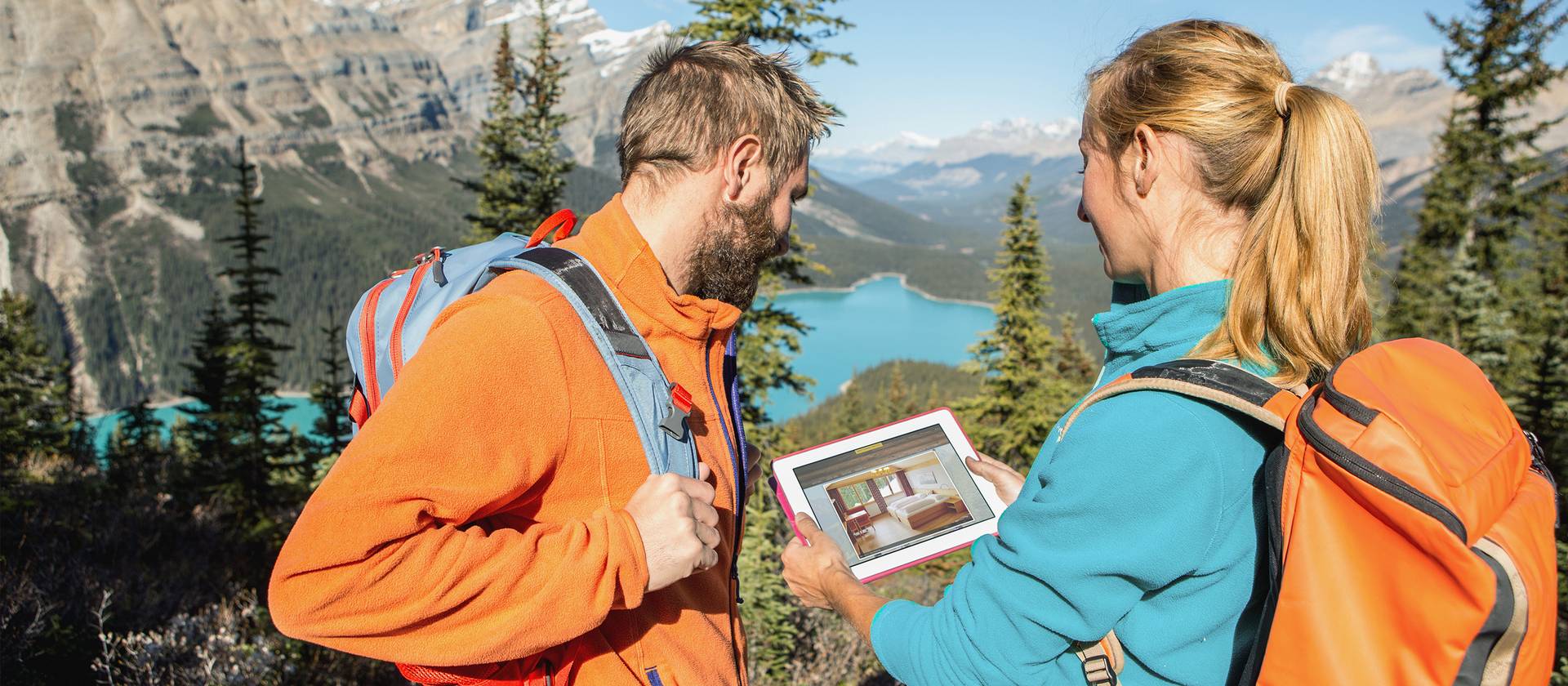 Imagebild Zwei Wanderer halten ein Tablet mit Blick auf einen Bergsee.