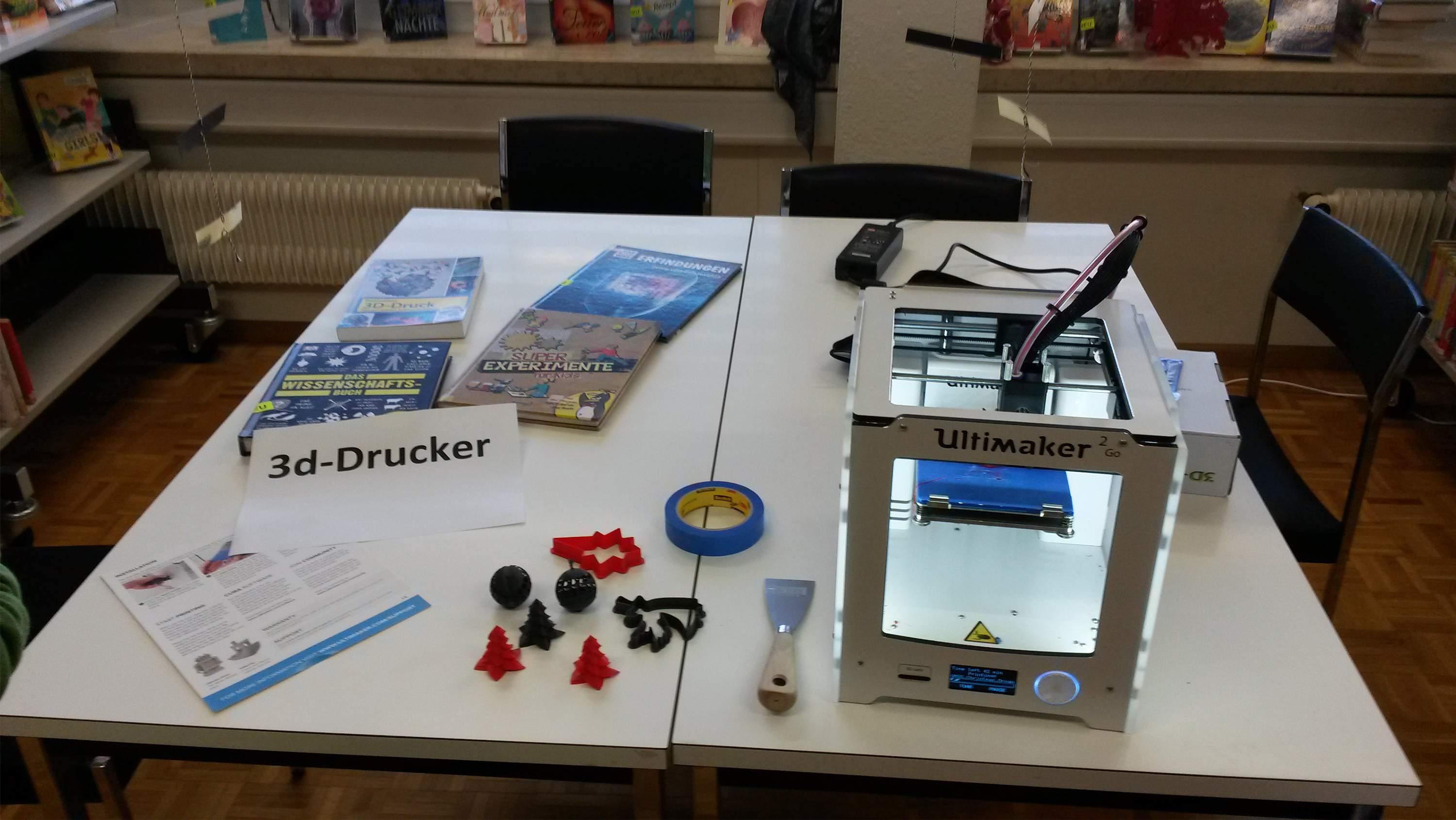 Tisch mit einem 3D-Drucker sowie Beispiele was damit gedruckt werden kann.