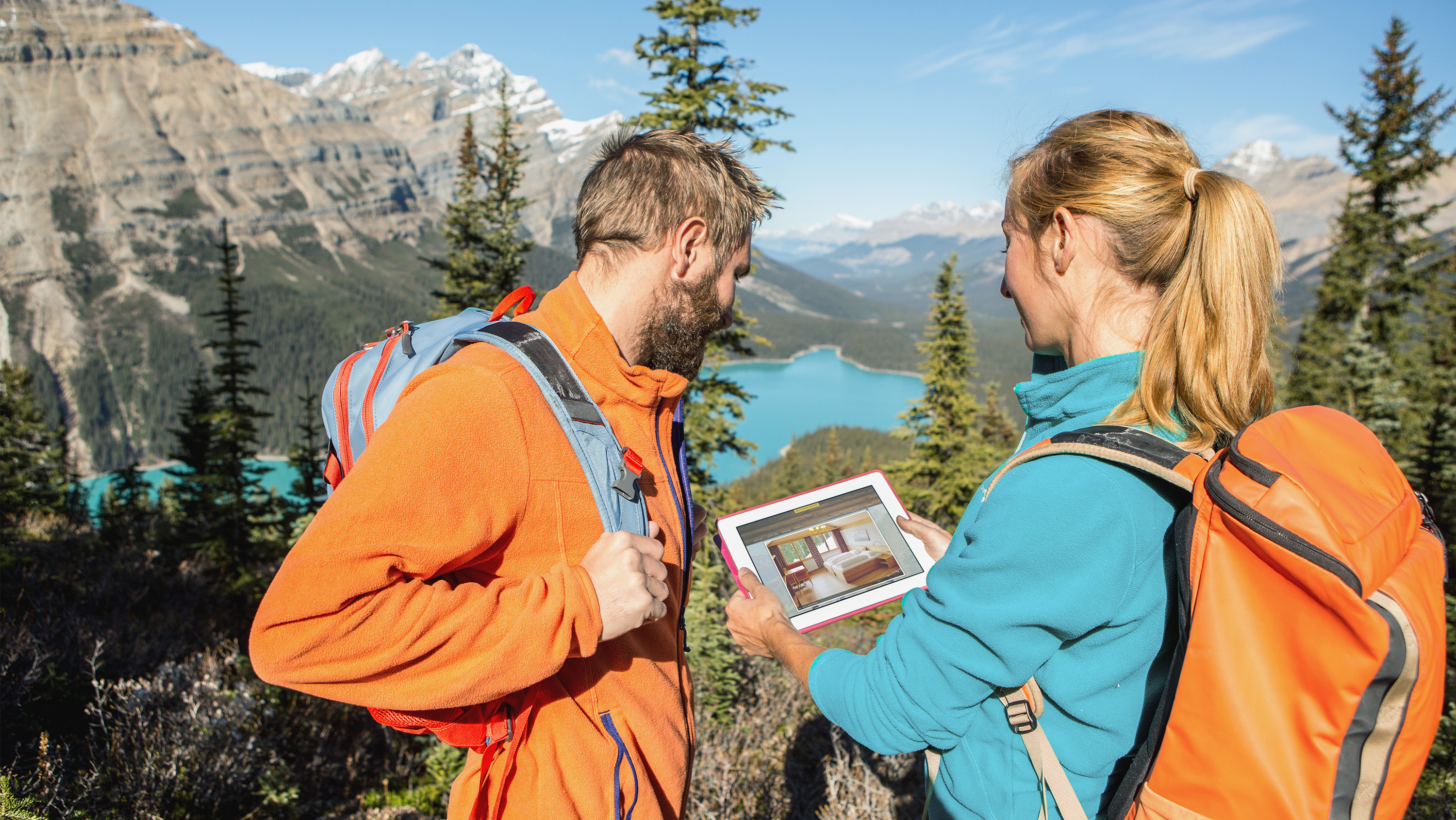 Imagebild Zwei Wanderer halten ein Tablet mit Blick auf einen Bergsee.